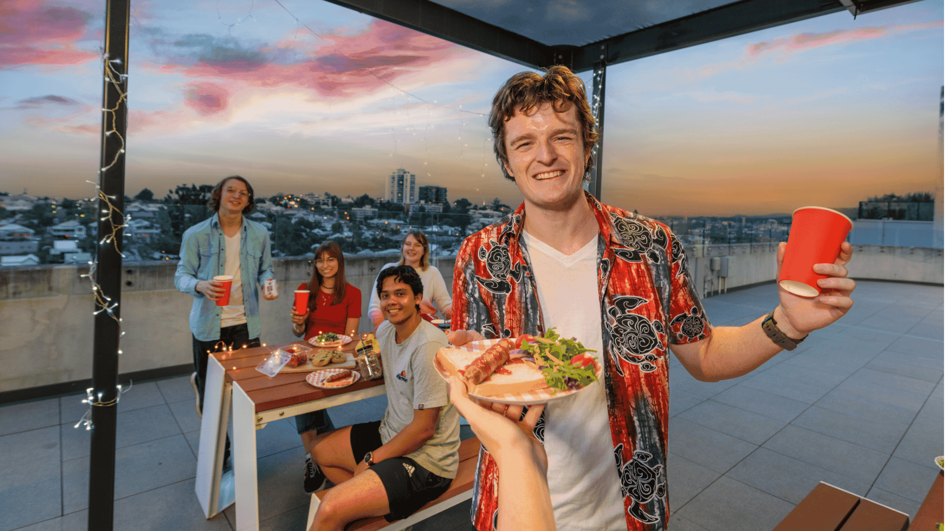 Young guests enjoying a rooftop barbecue gathering at sunset with city views at UniLodge South Bank