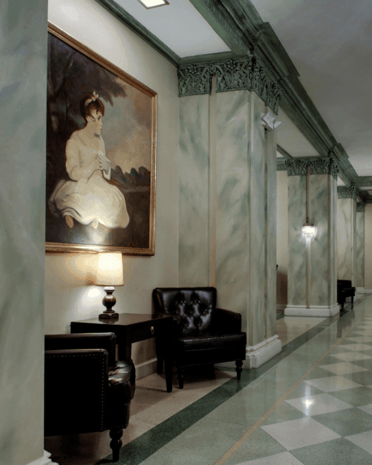 Elegant hallway at Knickerbocker On The Lake featuring a classic portrait, leather chairs, and marble floors