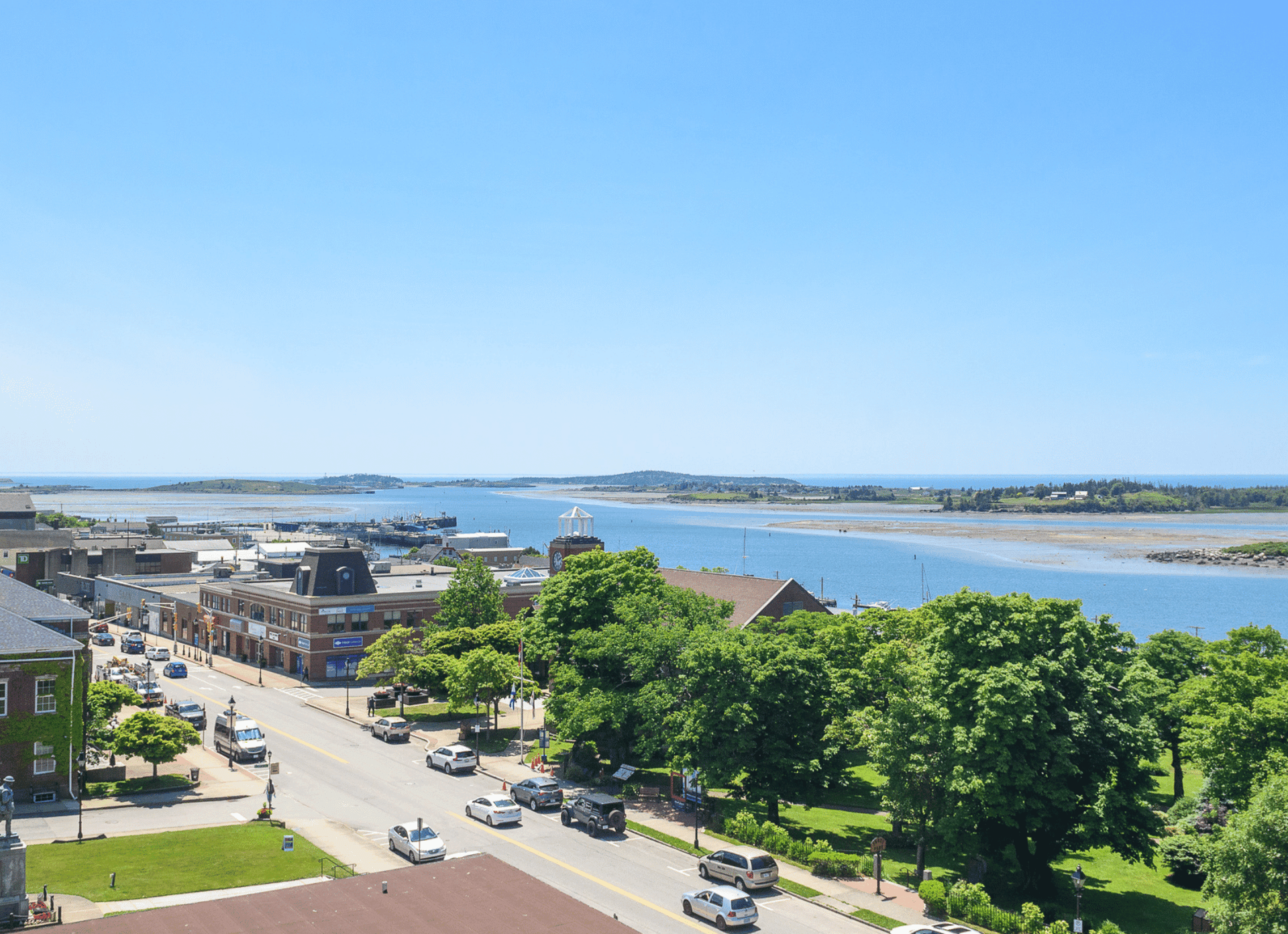High-angle view of a coastal town street with green trees and a blue bay in the distance near Rodd Grand Yarmouth