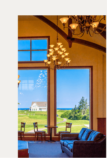 Ornate golden chandeliers hanging in a high-ceiling lounge overlooking golf course view atRodd Crowbush Golf & Beach Resort