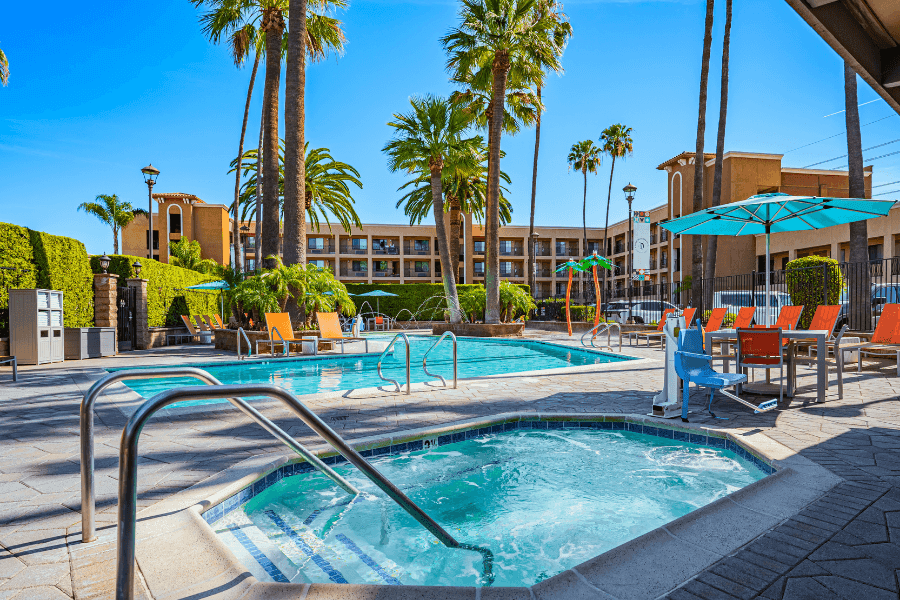 A pool and hot tub area with lounge chairs and palm trees