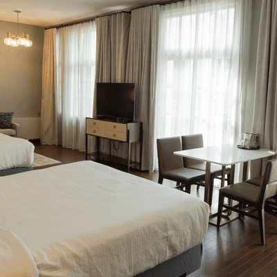 Bed facing small table set with chairs beside a window with TV, drapery in room at La Tourelle Hotel and Spa