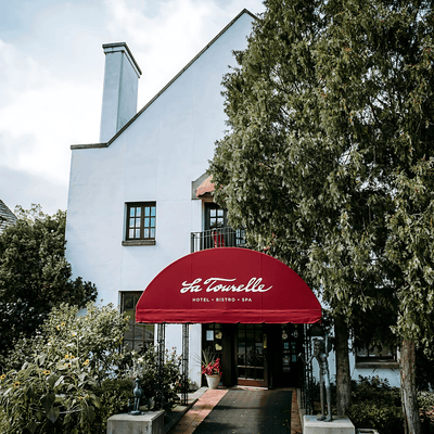 La Tourelle Hotel and Spa showcasing an entrance with a red canopy sign framed by surrounding trees and greenery
