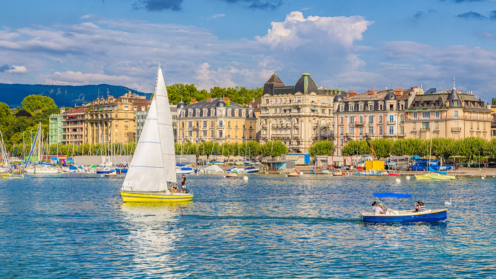 Sailboats glide through Geneva Lake near Warwick Hotels and Resorts with historical buildings and green trees under