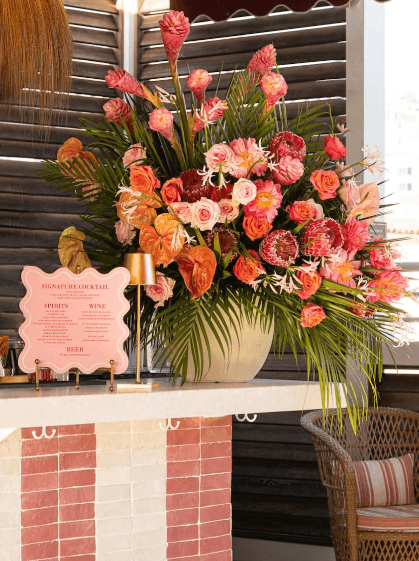 A bar with a large bouquet of flowers, a pink menu, and a wicker chair.