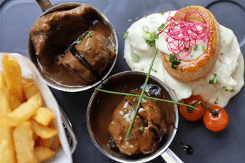 Gravy boats with tender meat alongside savory pastry and crispy fries on a dark surface at The Chutney\’s Restaurant