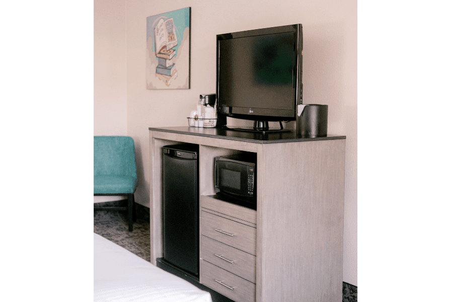 A hotel room with a television, mini fridge, microwave, and desk.