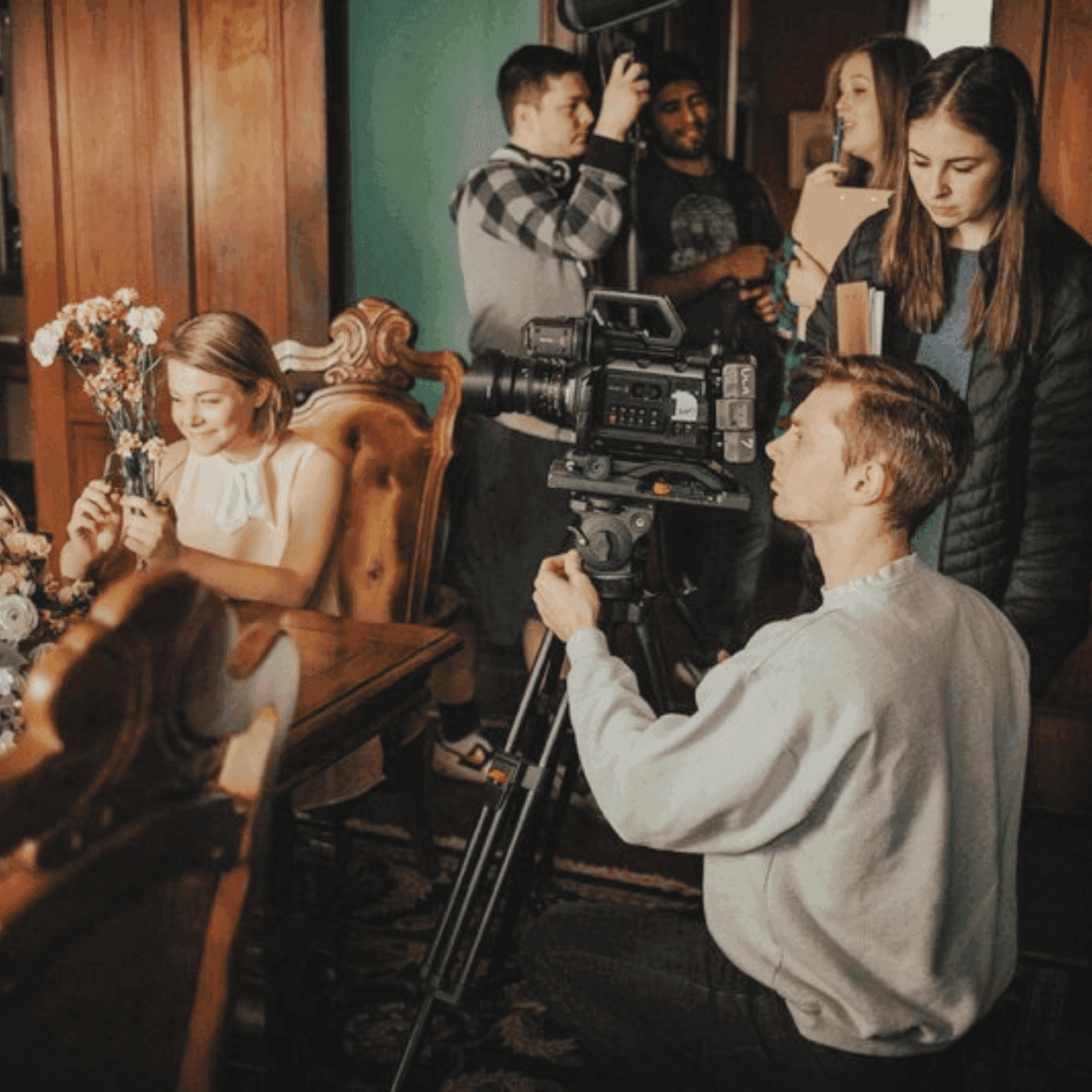 A group of people are filming a scene with a camera and tripod in a room.