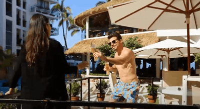 Man in sunglasses holding a drink by poolside bar with thatched roof and palm trees at Playa Los Arcos Puerto Vallarta