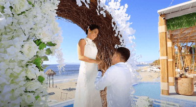 Man proposing to woman under white floral arch with ocean view at Playa Los Arcos Puerto Vallarta 2023