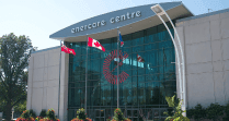 Glass facade of Enercare Centre building with Canadian flags on poles facing landscaping located beside Hotel X Toronto