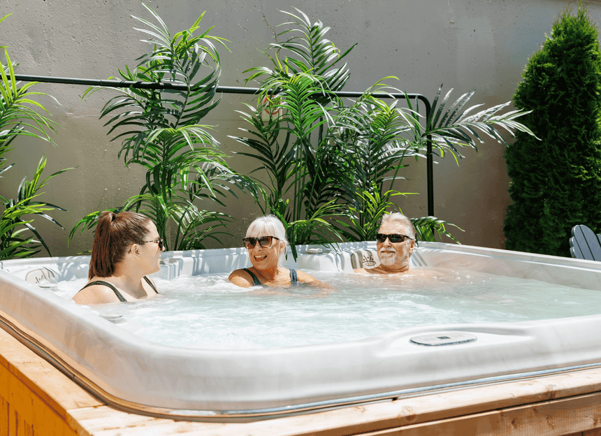 Three happy guests relaxing inside a steaming outdoor hot tub surrounded by lush green palm plants at Rodd Moncton