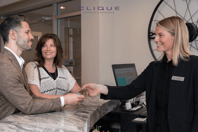 Friendly receptionist at a Clique Hotel & Resorts counter hands a key card to a smiling couple checking in