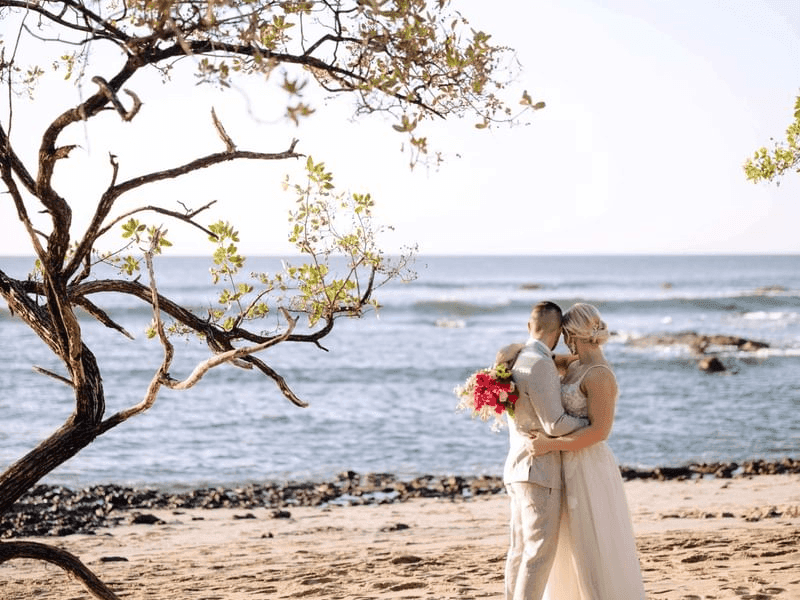 Newlyweds hugging on sandy beach by the ocean at the Cala Luna Hotel Boutique in Costa Rica.