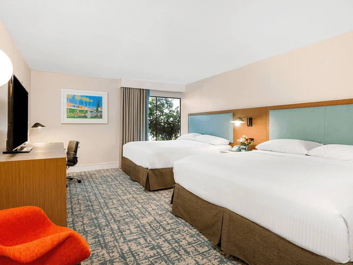 A hotel room with two beds, a desk, and a window.