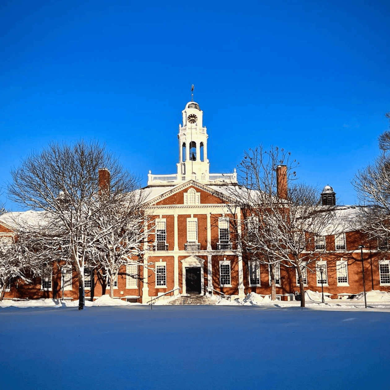 Historical brick building with clock tower and snowy surroundings in wintertime.