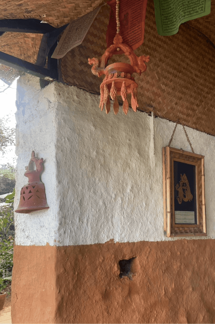 A rustic wall with traditional decorations, a bell, framed artwork, and a thatched roof at The Terraces Resort & Spa