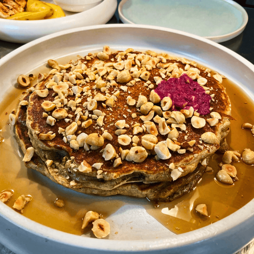 A plate of stacked tall griddle cakes topped with syrup and walnuts