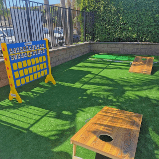 Outdoor game area with artificial turf featuring cornhole boards and a Connect Four game at Grand Legacy at The Park Anaheim