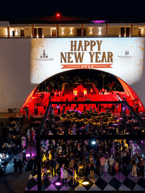 Aerial view of an elegant outdoor New Year's Eve celebration with illuminated stage, palm trees, and guests on a checkered floor.