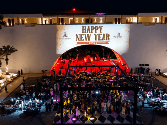 Aerial view of an elegant outdoor New Year's Eve celebration with illuminated stage, palm trees, and guests on a checkered floor.