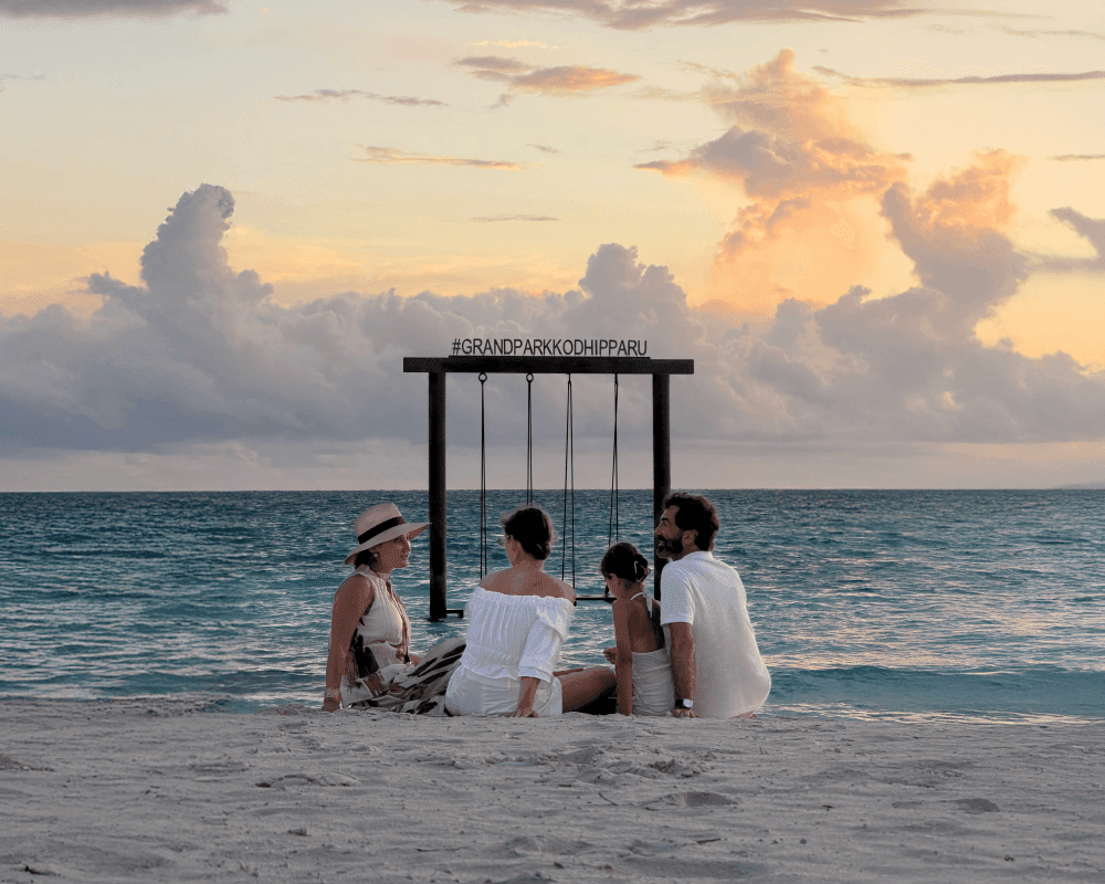 Grand Park Kodhipparu Maldives Family sitting down on the pristine beach with the sunset background