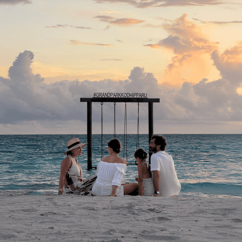 Family relaxing on beach at sunset with calm ocean and colorful clouds in the background