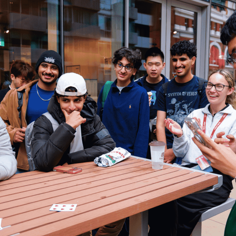 Group of students playing cards and socializing around an outdoor table at UniLodge student accommodation