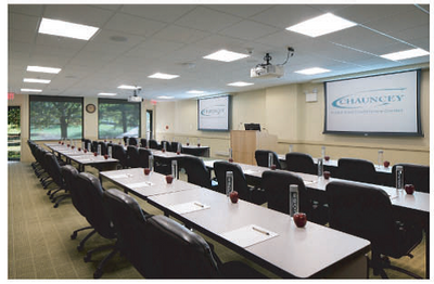 Conference room with long white tables, black chairs, and projection screens at Aramark Chauncey Conference Center