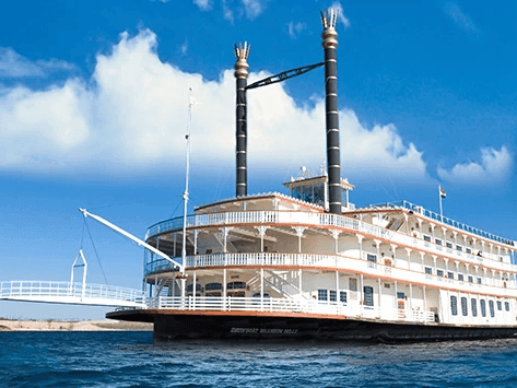 Large tiered riverboat with black smokestacks docked on calm blue water in Showboat Branson Belle near Branson Hillside Hotel