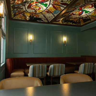 Dining seating area under a colorful stained glass ceiling with green accent walls at La Tourelle Hotel and Spa