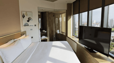 TV facing the cozy bed in The Mint Suite Bedroom with panoramic views of the city skyline at One Farrer Hotel