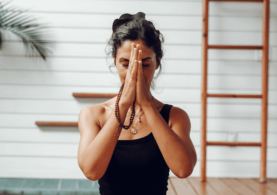 A woman with a brown rosary holding her hands together in prayer, practicing yoga at Ibagari Hotel