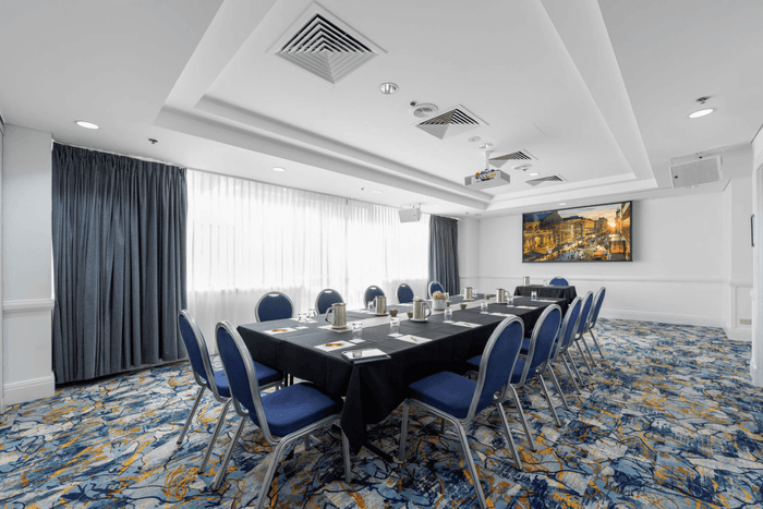 Blue and yellow carpeted conference room with blue chairs and a black table at Hotel Grand Chancellor Adelaide