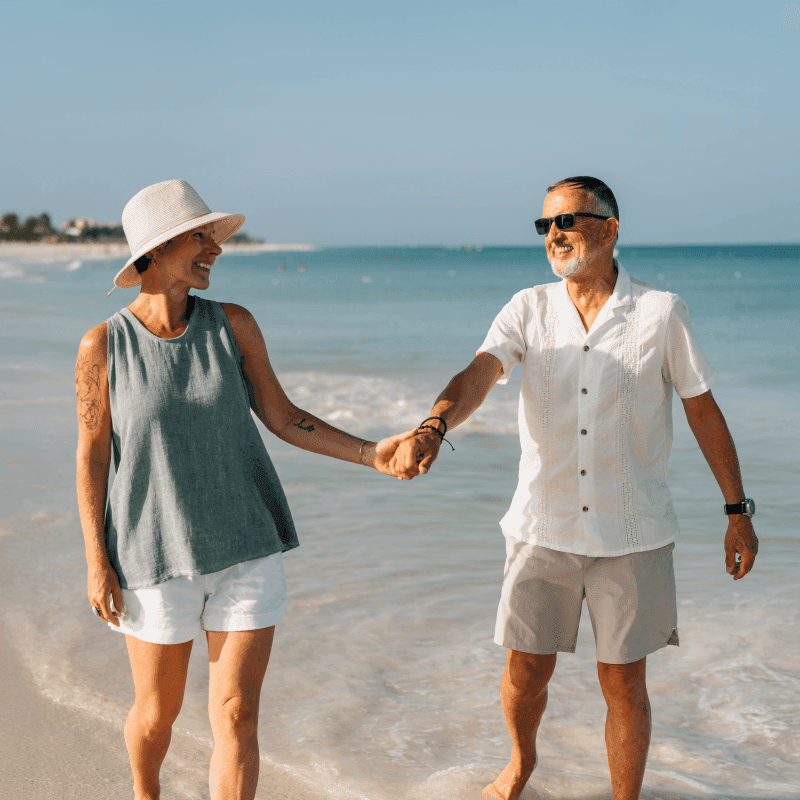 Elderly couple walking hand in hand on the beach, smiling and enjoying their summer holiday.