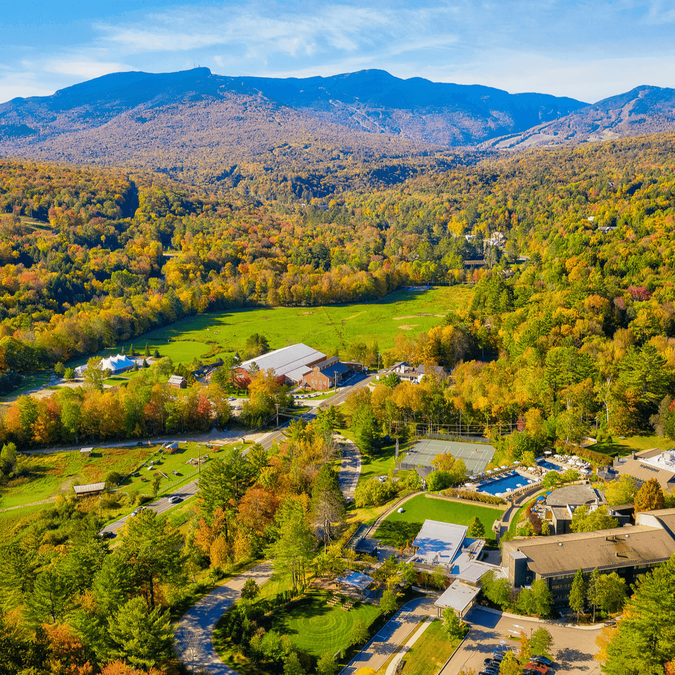 Aerial view of a resort with buildings, lush forest, and mountains in the background.