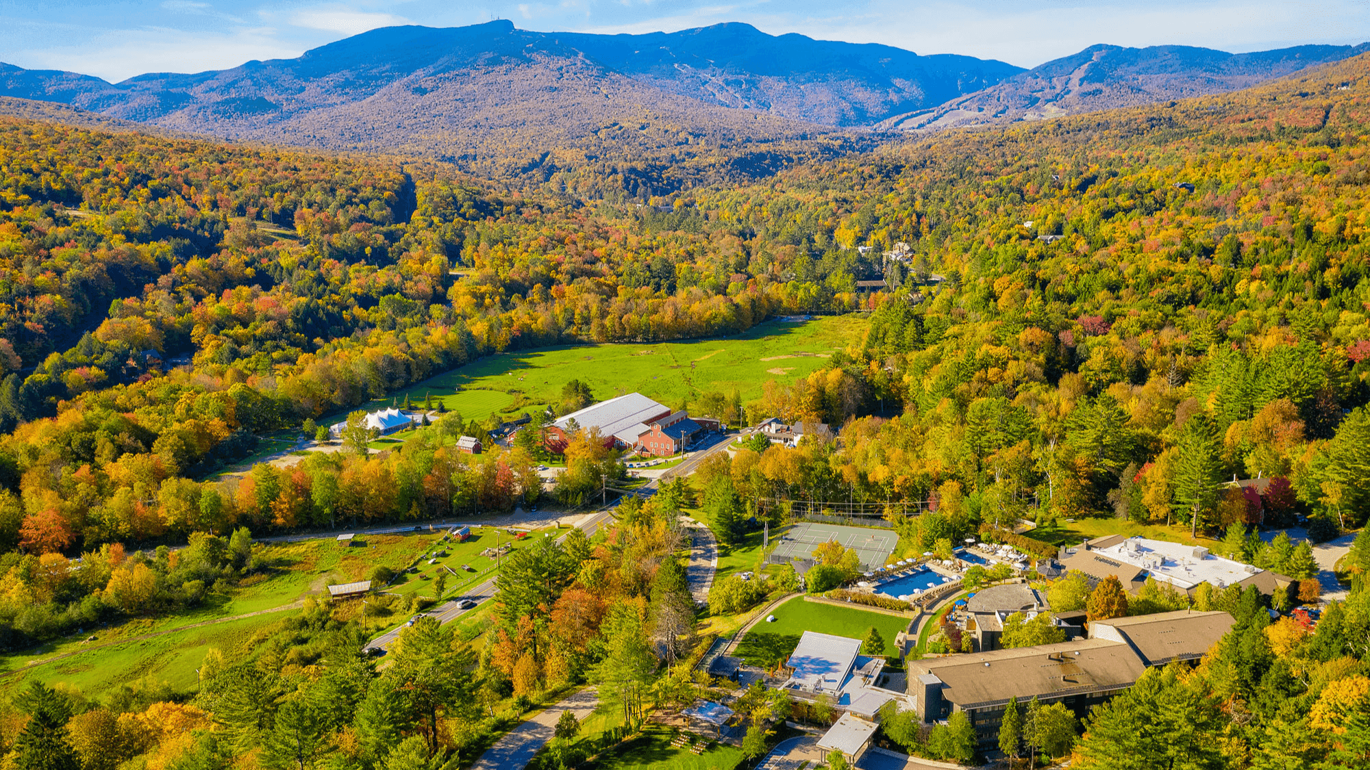 Aerial view of a resort with buildings, lush forest, and mountains in the background.