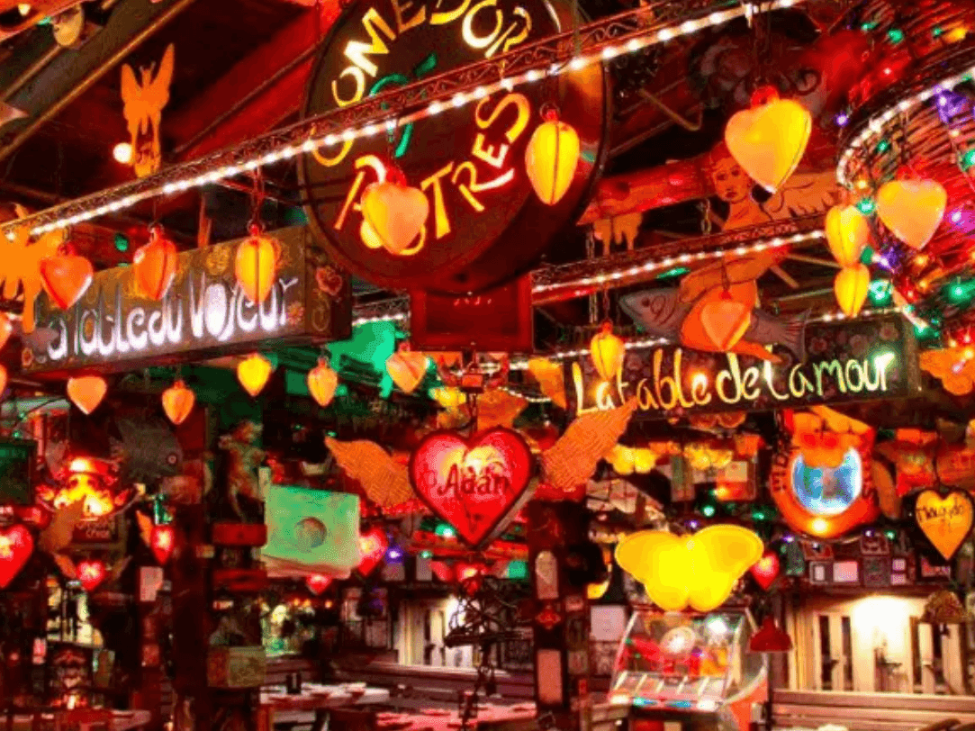 Interior de un restaurante vibrante con numerosas luces en forma de corazón, letreros eclécticos y adornos coloridos colgando del techo, creando un ambiente festivo.