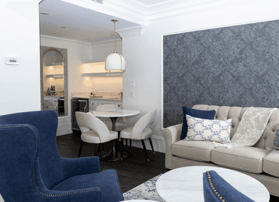 Modern suite living room with a plush grey sofa & blue armchairs, and a small dining table setup at Rodd Hotels & Resorts