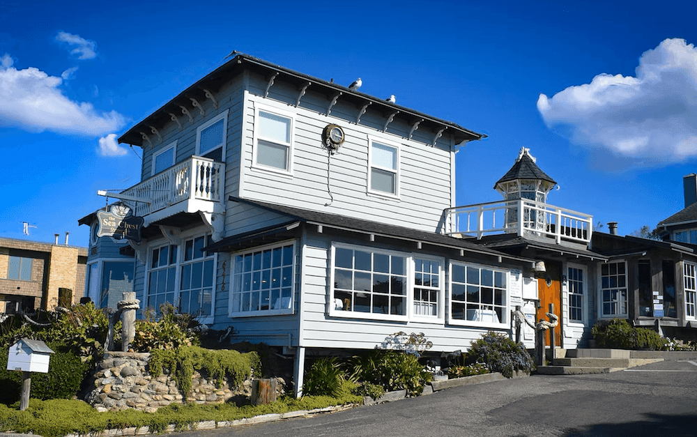 A two-story white building with a balcony and gardens under a blue sky with clouds.