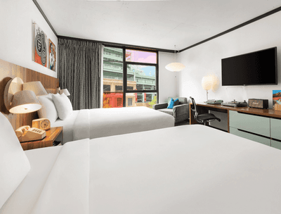 Two queen beds by the window and a TV with workspace in Stadium Queen at The Verb Hotel