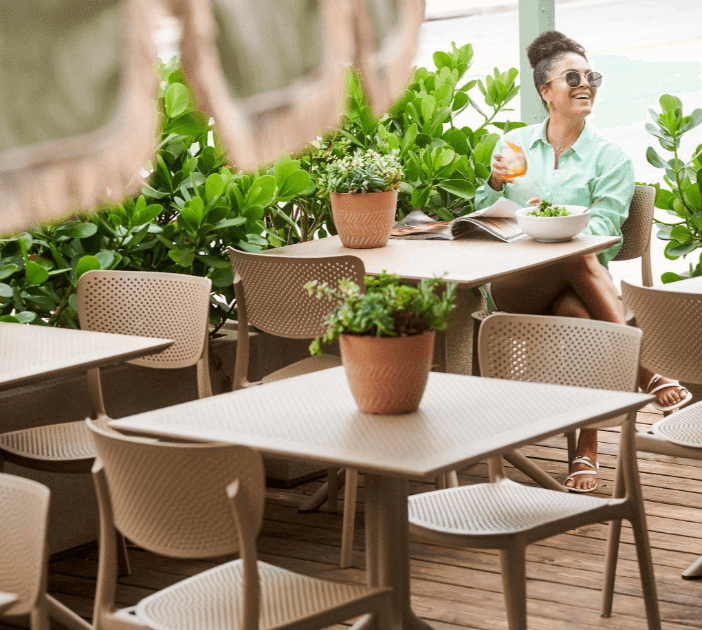 A woman sits at an outdoor dining table with a bowl of salad and a drink.