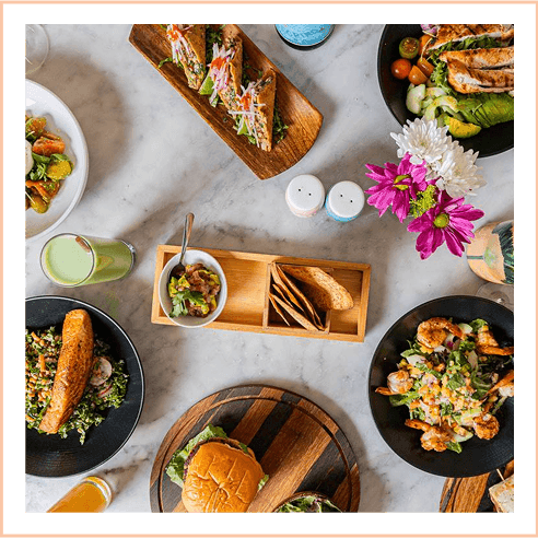 Overhead view of a table laden with fresh salads, salmon, a burger, and juice served at The Plymouth Hotel South Beach