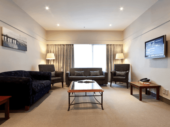 Living room with a wall-mounted TV and comfy sofas in the Family Room at James Cook Hotel Grand Chancellor