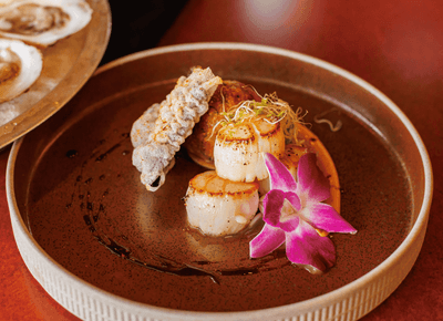 Seared scallops with crisp garnish and orchid arranged on a brown dining plate at Rodd Crowbush Golf & Beach Resort
