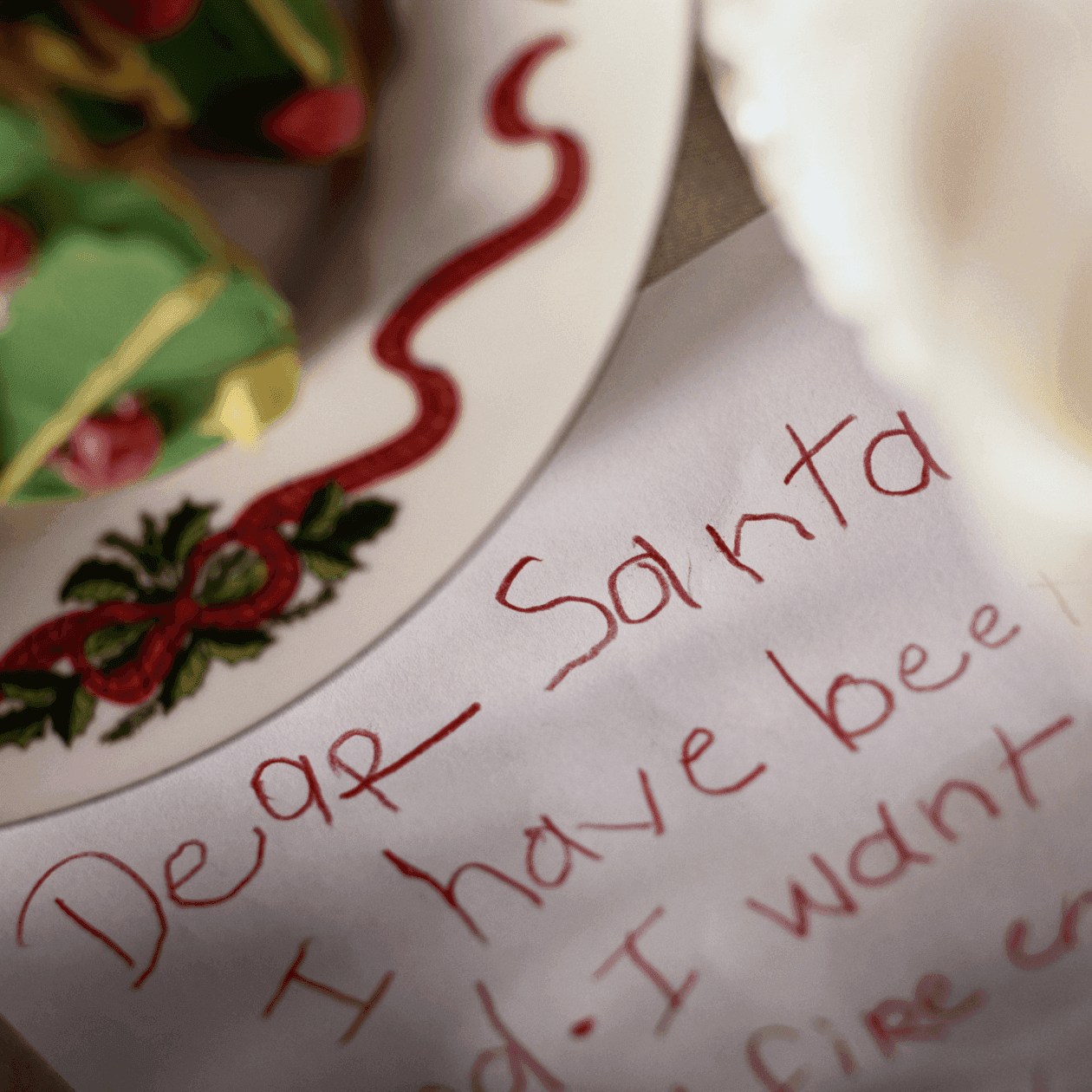 A close up of a hand written letter to Santa under a plate of christmas tree shaped cookies