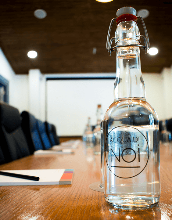 Water bottle on a wooden table by notebooks & chairs under warm lights in an event room at NOI Blend Colchagua