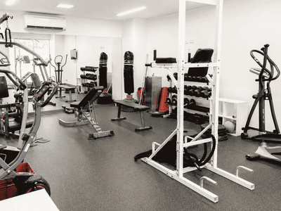 Modern fitness center with weight machines, free weights, cardio equipment, and exercise benches in a bright white room.