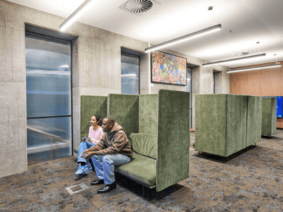 A lounge area with green booths, two people seated, and multiple gaming consoles present.