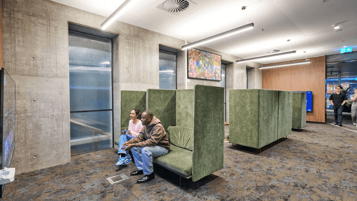 A lounge area with green booths, two people seated, and multiple gaming consoles present.